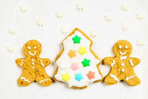 Gingerbread men friends at the Christmas tree on a white wooden