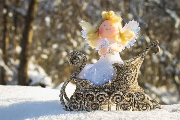 Игрушечный ангел сидит в золотых санях на снегу. Рождественские игрушки . — стоковое фото