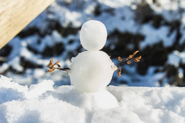 一个小雪人, 手里拿着树枝, 站在阳光下的雪地里. — 图库照片