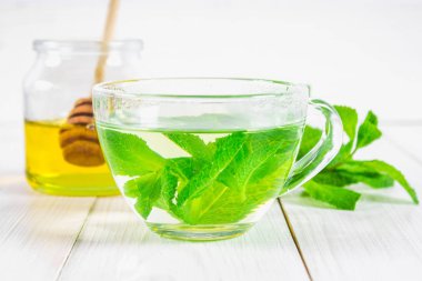 Bal kavanozu Beyaz ahşap bir masa üzerinde bir fincan nane çayı.