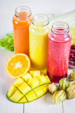 Mango, portakal, muz, kereviz, çilek, ahşap bir masa üzerinde şişelerde çok renkli smoothies.