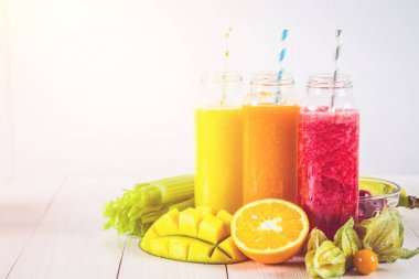 Mango, portakal, muz, kereviz, çilek, ahşap bir masa üzerinde şişelerde çok renkli smoothies.