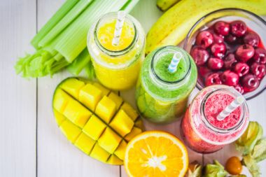 Mango, portakal, muz, kereviz, çilek, ahşap bir masa üzerinde şişelerde çok renkli smoothies.