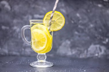 Bir bardak kulplu gri beton zemin üzerine ev yapımı limonata. Karanlık bir arka plan üzerinde limon dilimleri ile su.