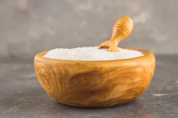 Azúcar blanco en un plato de madera con un basurero sobre un fondo oscuro . — Foto de Stock