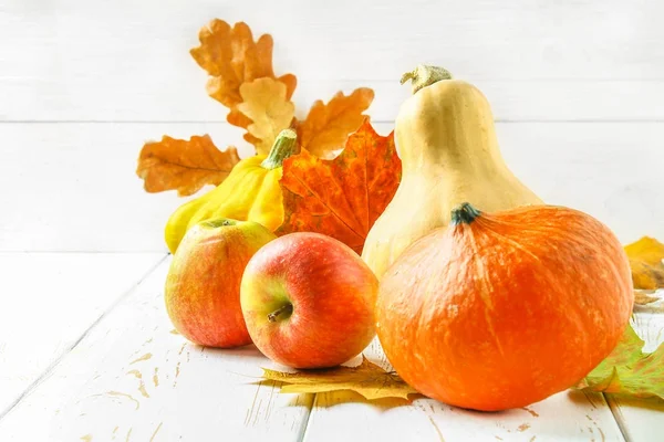 Pumpkin and patty pan, apples and maple, oak yellow leaves on a white wooden table. Autumn harvest.