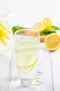 Bir cam kabı ve bir sürahi soğuk limonata limon tarafından çevrili beyaz ahşap zemin üzerinde.