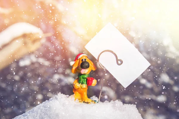 Игрушечная собака с белым чистым листом - символ нового года в снегу. Рождественские игрушки . — стоковое фото
