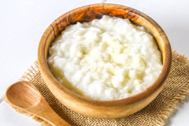 Pirinç sütü yulaf lapası ile fındık ve kuru üzüm bir beyaz tahta masada ahşap kase.