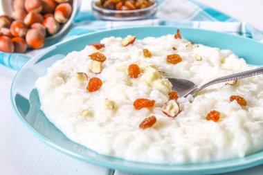 Pirinç sütü yulaf lapası ile fındık ve kuru üzüm Beyaz ahşap bir masa üzerinde mavi bir tabak içinde.