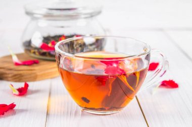 Bir fincan çay, siyah bir bitki çiçek çayı ile banka beyaz ahşap bir masa üzerinde arka planda.