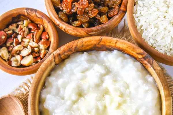 Gachas de leche de arroz con nueces y pasas en tazones de madera sobre una mesa de madera blanca . — Foto de Stock