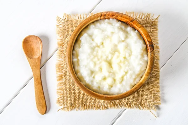 Pirinç sütü yulaf lapası ile fındık ve kuru üzüm bir beyaz tahta masada ahşap kase. — Stok fotoğraf