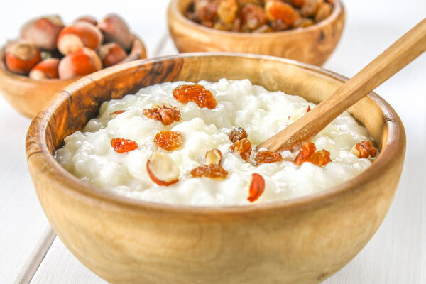 Rice milk porridge with nuts and raisins in wooden bowls on a white wooden table.