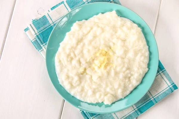 Mingau de leite de arroz com nozes e passas em um prato azul em uma mesa de madeira branca . — Fotografia de Stock