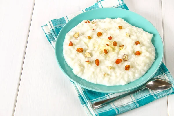 Porridge di latte di riso con noci e uva passa in un piatto azzurro su un whi — Foto Stock