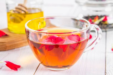 Bir fincan çay, bal ve bir kavanoz siyah bir bitki çiçek çayı ile bir banka beyaz ahşap bir masa üzerinde arka planda.