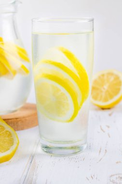 Bir cam kabı ve bir sürahi soğuk limonata limon tarafından çevrili beyaz ahşap zemin üzerinde.