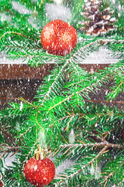 Bolas rojas de Navidad y conos se encuentran en un estante marrón de madera rodeado de ramas de abeto . —  Fotos de Stock