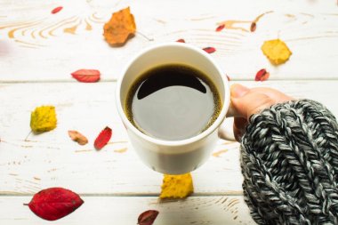 Bir kadının elinde bir kazak örme bir eşarp ile ahşap bir masa üzerinde sonbahar ortamda sıcak kahve bir fincan kazak. Konfor, sıcaklık, rahat.