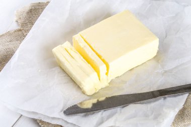 Beyaz bir tablo üzerinde bir bıçak ile ahşap bir tahta üzerine tereyağı bir bar. Yemek pişirmek için malzemeler.