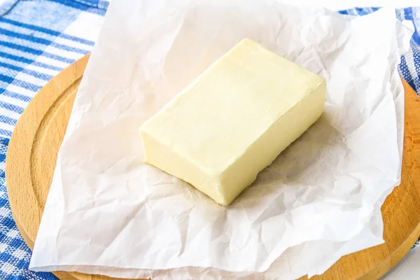 Una barra de mantequilla en una tabla de madera con un cuchillo, sobre una mesa blanca. Ingredientes para cocinar . — Foto de Stock