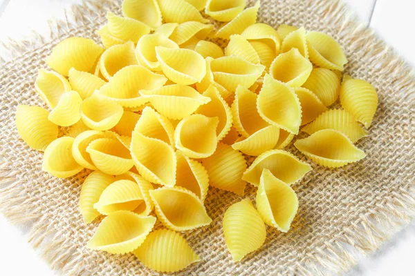 Culinaire achtergrond met conchiglie pasta op houten tafel. Pasta in de vorm van zeeschelpen op een zak met peterselie. — Stockfoto