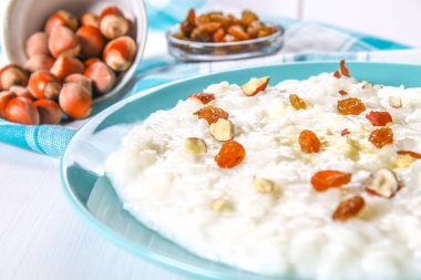 Pirinç sütü yulaf lapası ile fındık ve kuru üzüm Beyaz ahşap bir masa üzerinde mavi bir tabak içinde.