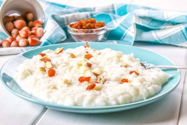 Pirinç sütü yulaf lapası ile fındık ve kuru üzüm Beyaz ahşap bir masa üzerinde mavi bir tabak içinde.