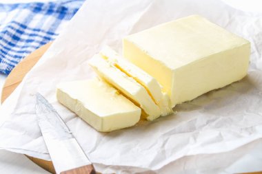 Beyaz bir tablo üzerinde bir bıçak ile ahşap bir tahta üzerine tereyağı bir bar. Yemek pişirmek için malzemeler.
