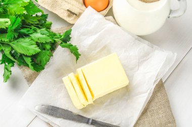 Bir kalıp tereyağı süt, yumurta ve maydanoz beyaz bir tablo çevrili bir bıçakla bir ahşap tahta üzerinde parçalar halinde kesin. Yemek pişirmek için malzemeler.