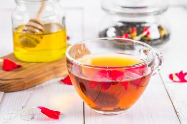 Bir fincan çay, bal ve bir kavanoz siyah bir bitki çiçek çayı ile bir banka beyaz ahşap bir masa üzerinde arka planda.