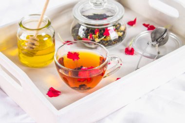 Bir fincan çay, bal konservesi ve bir kavanoz yatakta beyaz bir tepsi üzerinde siyah bitkisel çay.