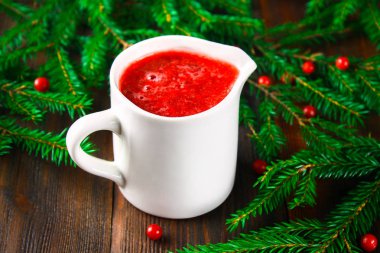 Fuska kızılcık sosuna çam dalları ile ahşap bir masa üzerinde bir cam beyaz sauceboat.