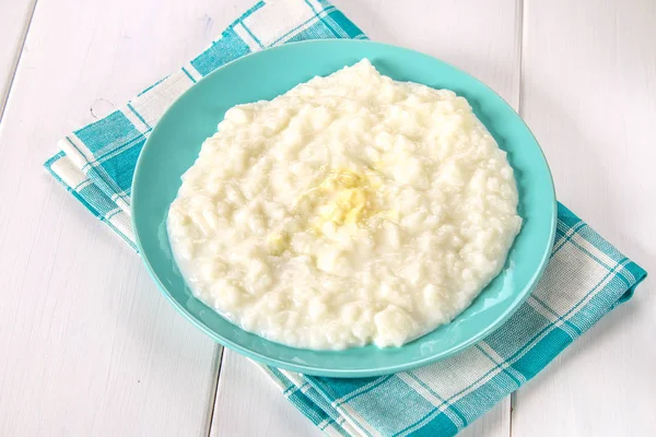 Pirinç sütü yulaf lapası ile fındık ve kuru üzüm Beyaz ahşap bir masa üzerinde mavi bir tabak içinde. — Stok fotoğraf