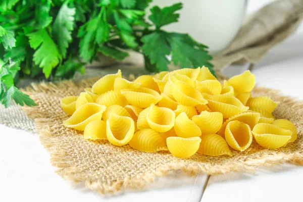 Fondo culinario con pasta conchiglie sobre mesa de madera. La pasta en forma de las conchas marinas en el saco con el perejil . — Foto de Stock