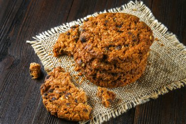 Ev yapımı yulaf ezmeli kurabiye. Çuval bezi kahverengi ahşap bir masa üzerinde çerezleri yığını. Süt içinde belgili tanımlık geçmiş.