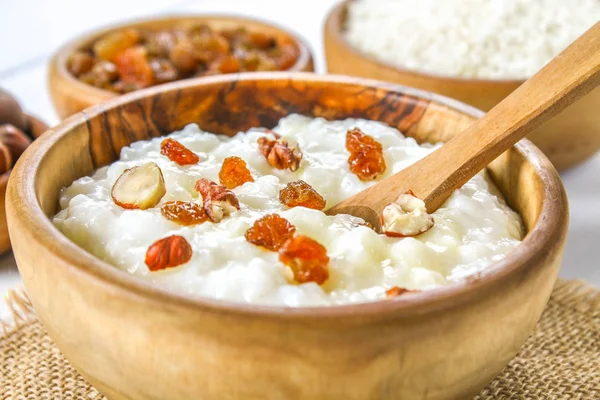 Rijst melk havermoutpap met noten en rozijnen in houten schalen op een witte houten tafel. — Stockfoto