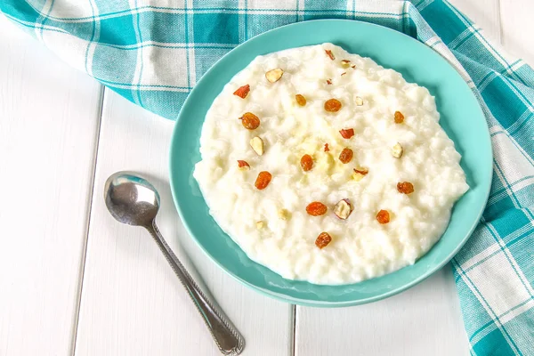 Porridge di latte di riso con noci e uva passa in un piatto azzurro su un whi — Foto Stock