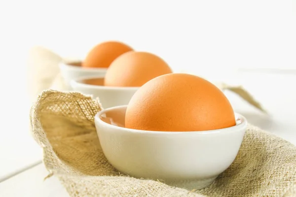 Raw hnědé slepičí vejce ve skleněné mísy na bílý dřevěný stůl. Ingredience pro vaření. — Stock fotografie