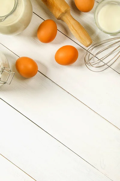 Ωμό καφέ κοτόπουλο αυγά, γάλα, ζάχαρη, αλεύρι, σύρμα, τροχαίο καρφίτσα σε ένα λευκό ξύλινο τραπέζι. Υλικά για το μαγείρεμα. — Φωτογραφία Αρχείου