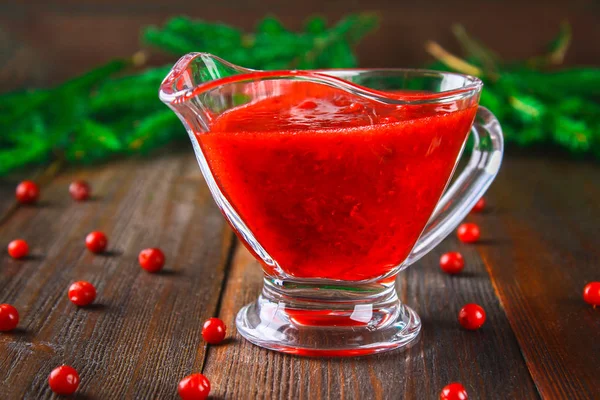 Salsa de arándano de fresa en un platillo transparente de vidrio sobre una mesa de madera con ramas de abeto . — Foto de Stock