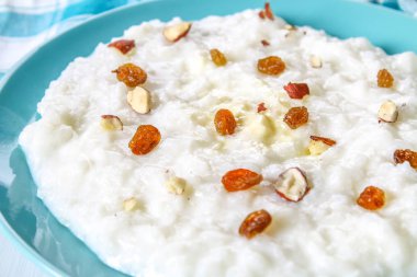 Pirinç sütü yulaf lapası ile fındık ve kuru üzüm Beyaz ahşap bir masa üzerinde mavi bir tabak içinde.