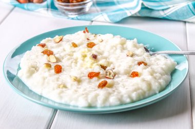 Pirinç sütü yulaf lapası ile fındık ve kuru üzüm Beyaz ahşap bir masa üzerinde mavi bir tabak içinde.