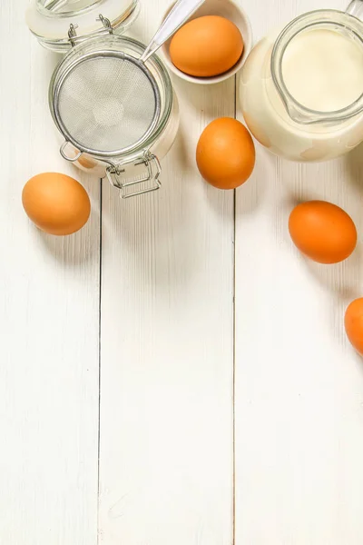 Ωμό καφέ κοτόπουλο αυγά, γάλα, ζάχαρη, αλεύρι, σύρμα, τροχαίο καρφίτσα σε ένα λευκό ξύλινο τραπέζι. Υλικά για το μαγείρεμα. — Φωτογραφία Αρχείου