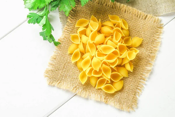 Fond culinaire avec pâtes conchiglie sur table en bois. Pâtes sous forme de coquillages sur un sac de persil . — Photo