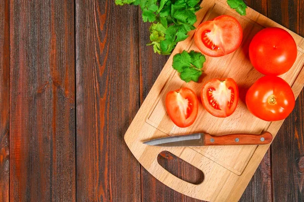 Świeże pomidory czerwone i plasterki połówki z kolendry na drewnianym stole. Widok z góry. — Zdjęcie stockowe