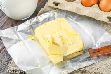 Bir kalıp tereyağı süt, yumurta ve maydanoz kahverengi bir tabloda çevrili bir bıçakla bir ahşap tahta üzerinde parçalar halinde kesin. Yemek pişirmek için malzemeler.