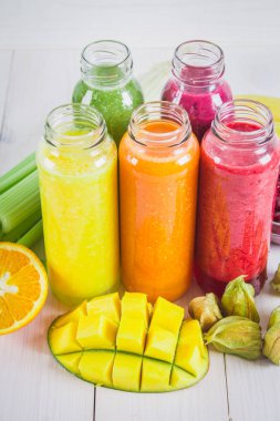 Mango, portakal, muz, kereviz, çilek, ahşap bir masa üzerinde şişelerde çok renkli smoothies.