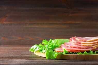 Taze yeşil salata ile dilimlenmiş jambon yuvarlak kesme tahtası üzerinde bırakır. Et ürünleri bir kahverengi ahşap tablo.